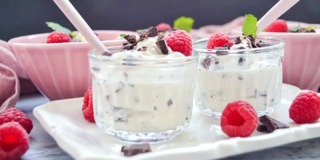 Zwei Gläschen mit cremigem Dessert, garniert mit Himbeeren und Schokostückchen. Ein köstliches Herrencreme Rezept zum Genießen.