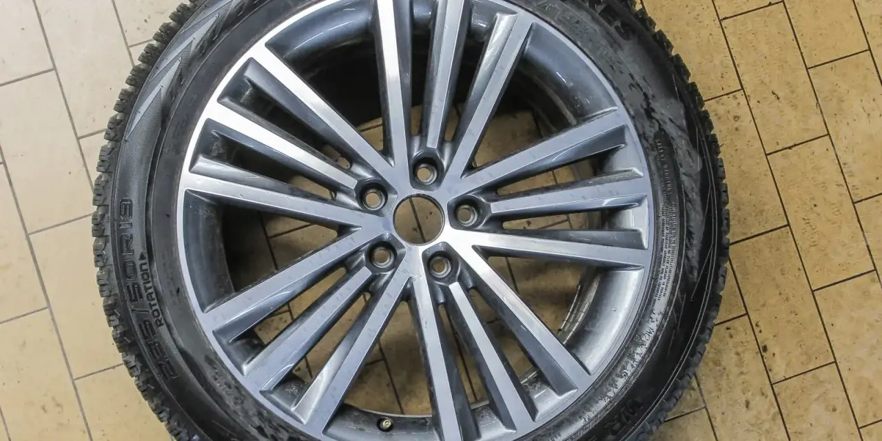 Felga aluminiowa z oponą zimową na tle kafelków.
