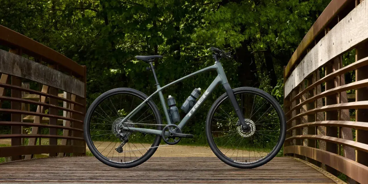 A grey Trek bike sits on a wooden bridge, ready for road or mountain biking adventures through the lush green forest.