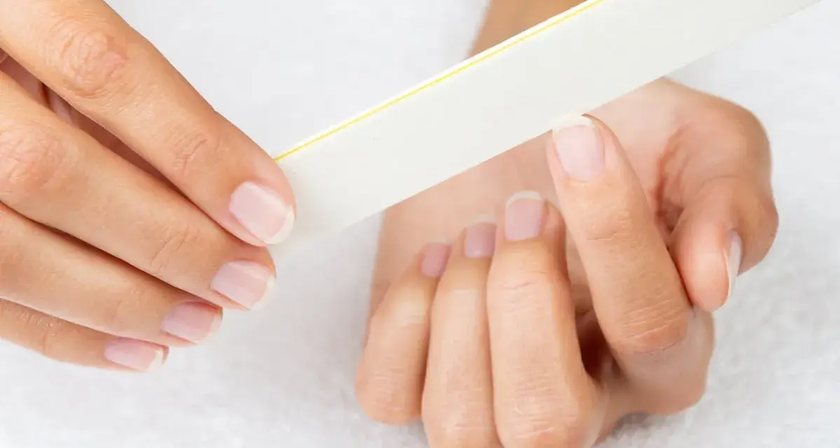 Une main lime délicatement ses ongles, comme un remède de grand-mère pour un ongle abîmé.