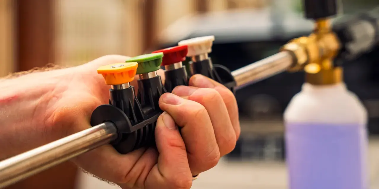 Choosing the right nozzle to pressure wash car is key. This hand holds a selection of colored tips for a pressure washer wand, ready for detailing.