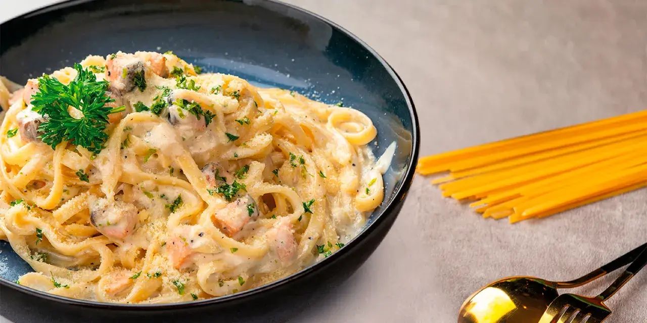 Pasta cremosa con trozos de salmón y perejil, servida en un plato azul oscuro.