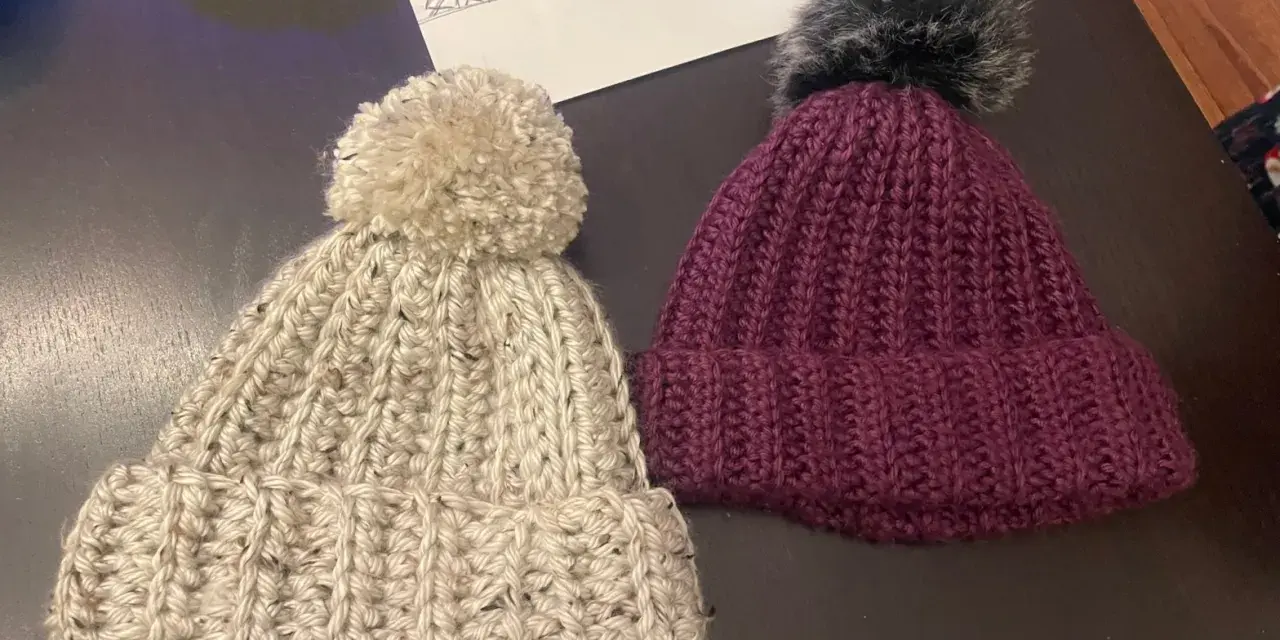 Dwie ręcznie robione czapki z pomponami: beżowa i bordowa.