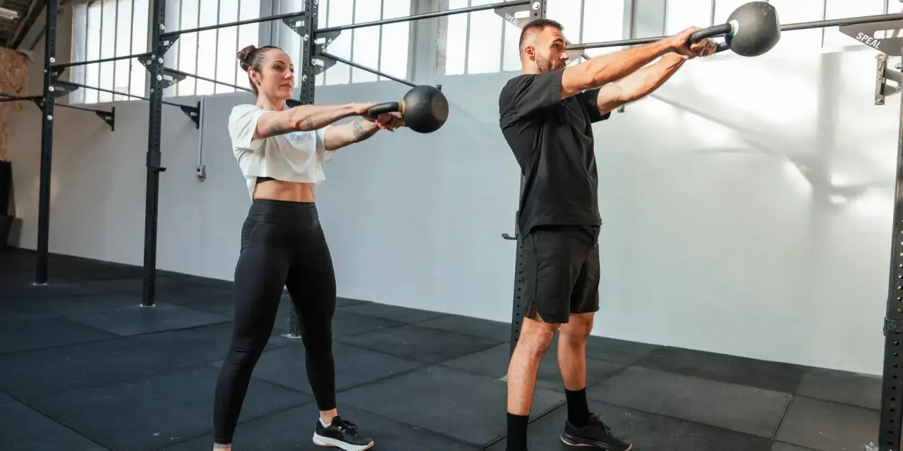 Kobieta i mężczyzna wykonują ćwiczenia z kettlebellami w siłowni.