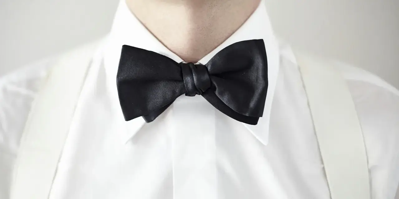 Elegancki mężczyzna w białej koszuli z czarną muszką i białymi szelkami. Kołnierzyk półwłoski idealnie dopełnia stylizację.