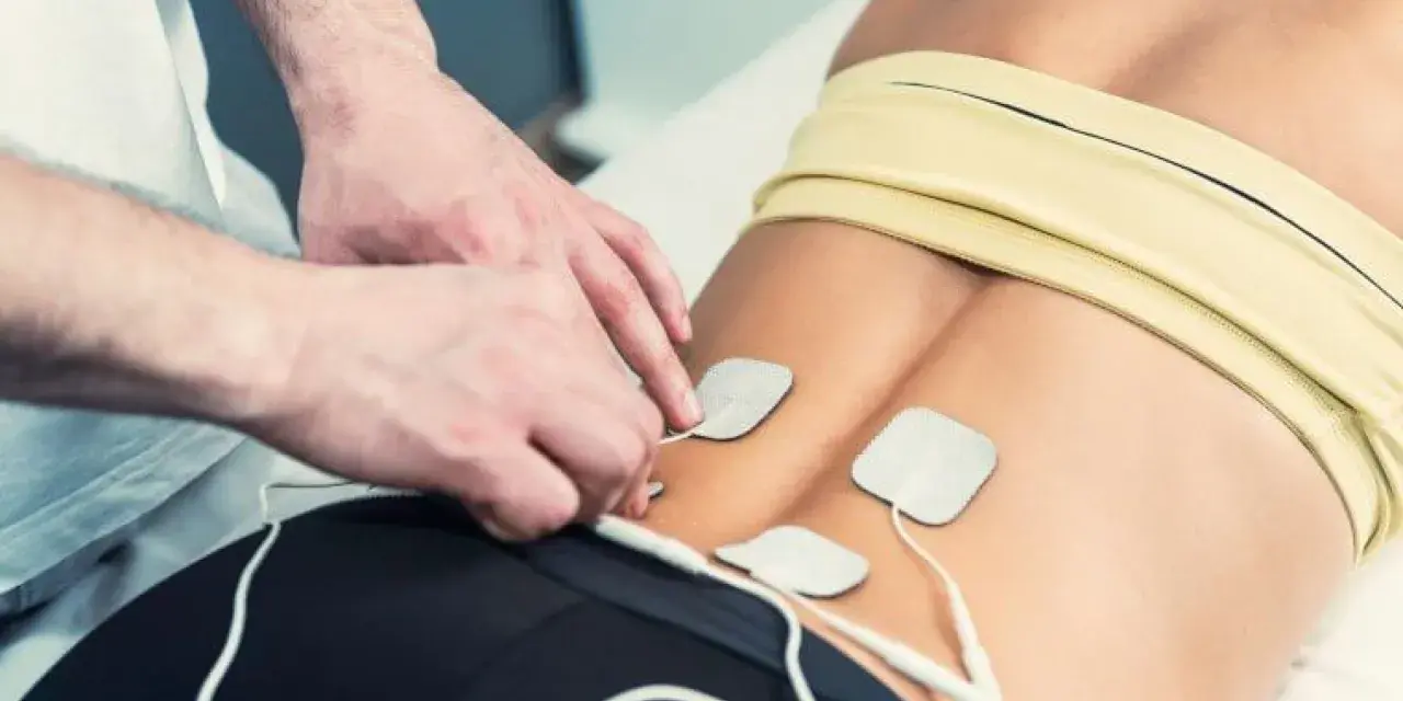 Fysioterapeut applicerar elektroder för elbehandling av muskler i ländryggen.