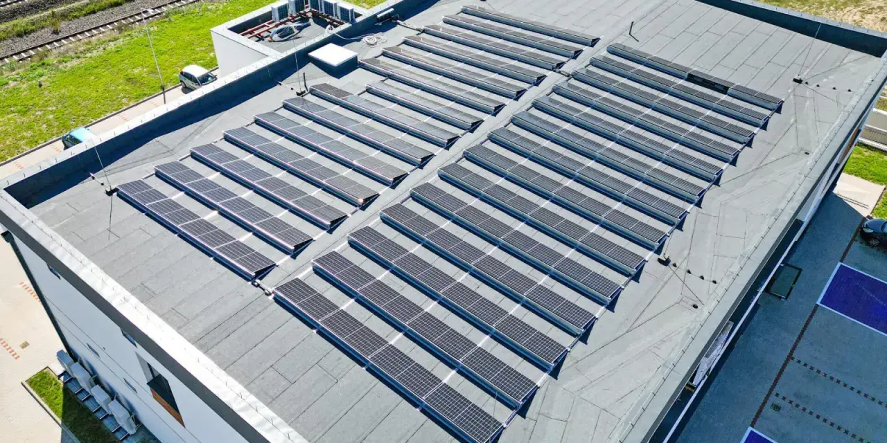 Duży dach płaski pokryty panelami fotowoltaicznymi, które zbierają energię słoneczną.