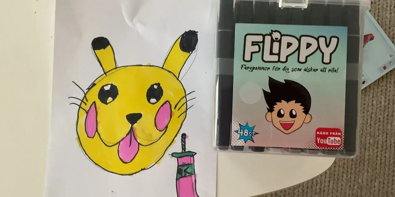 En gul Pikachu-liknande figur med rosa kinder och en tunga som sticker ut, bredvid en låda med färgpennor "FLIPPY" för dig som älskar att rita.