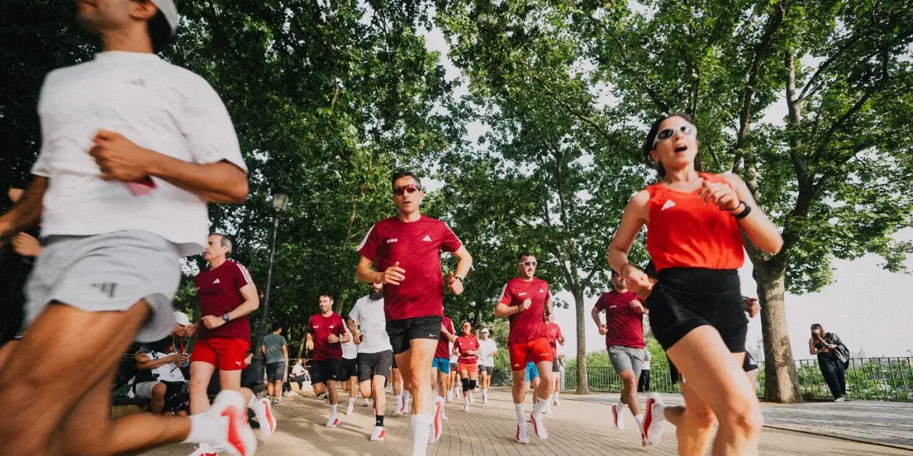 Corredores entrenan para el maratón Madrid 2026 en un día soleado, bajo la sombra de árboles frondosos.