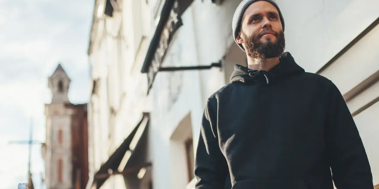 Mężczyzna w czarnej bluzie z kapturem i czapce beanie patrzy w górę. Stylowy sposób, jak nosić bluzę z kapturem.