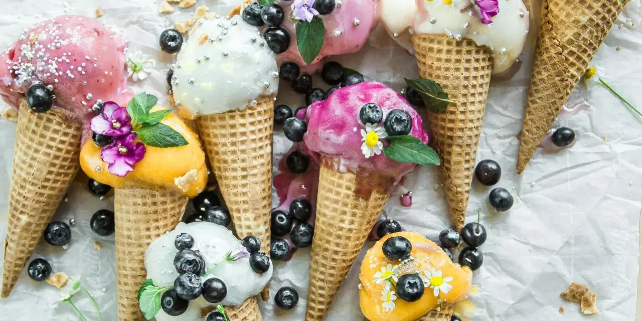 Bunte Eistüten mit Blaubeeren und Blüten. Wer fragt sich, wie viel Kalorien hat eine Kugel Eis, wenn sie so verlockend aussieht?