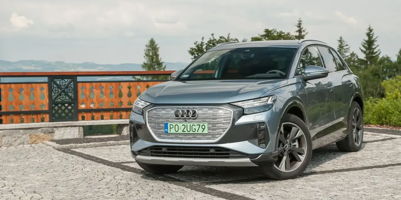 Szary Audi Q4 na kamienistym podjeździe, z widokiem na góry i las.