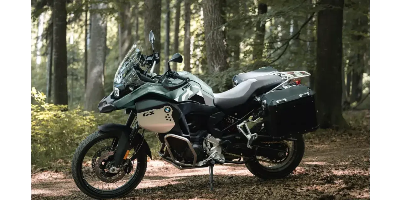 Zielony motocykl BMW F900GS z kuframi, gotowy na przygodę w lesie.