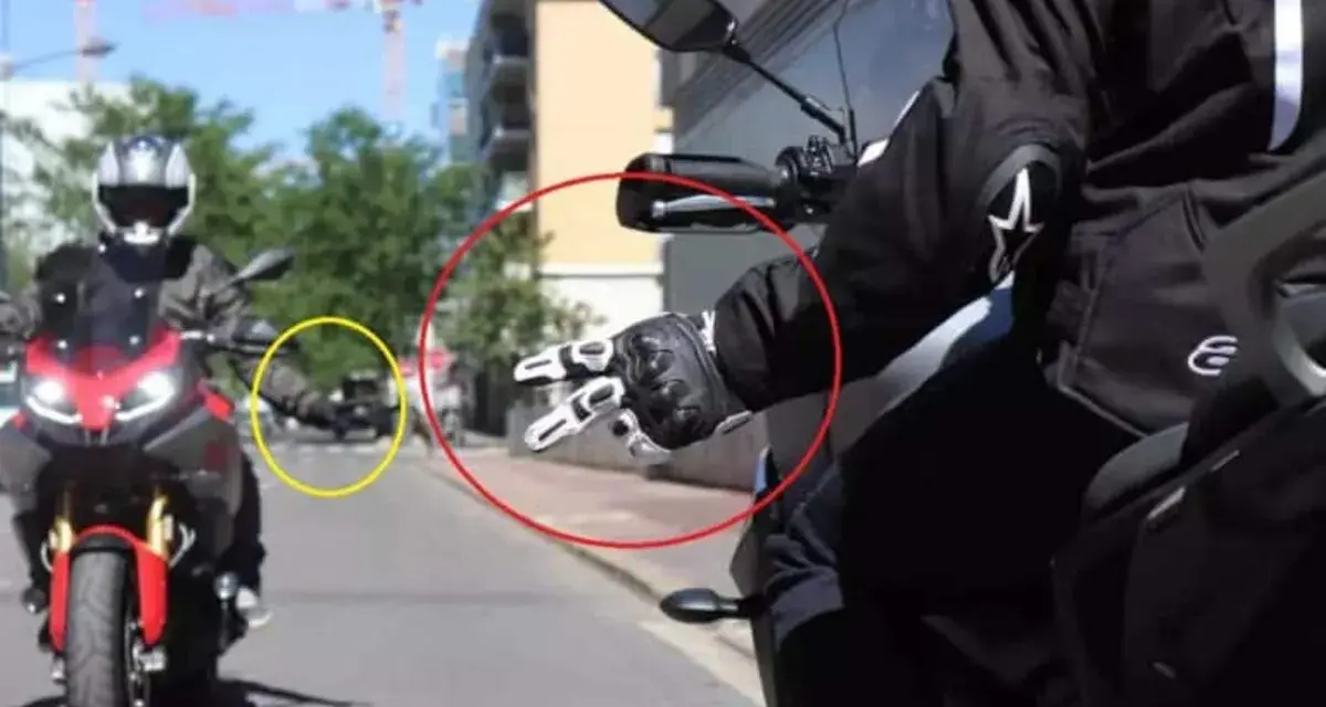 Mano guantata che fa il segno di pace, un gesto del linguaggio motociclisti. Un'altra moto in lontananza.