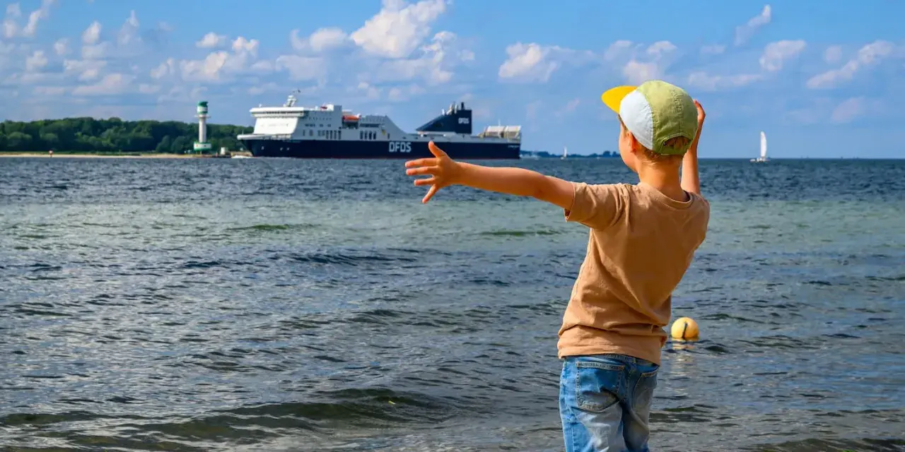 Kind winkt einem großen Schiff in Flensburg zu. Ein toller Ausflug mit Kindern, auch wenn es mal regnet.