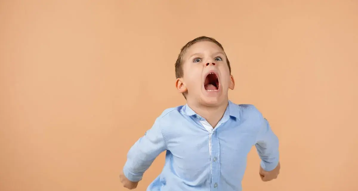 Bambino con espressione di forte frustrazione, con bocca spalancata e pugni chiusi. Un'immagine che evoca la necessità di capire come calmare un bambino autistico.