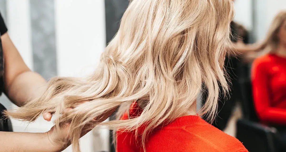 Fryzjerka pokazuje klientce, jak obciąć włosy, prezentując pasmo blond włosów.
