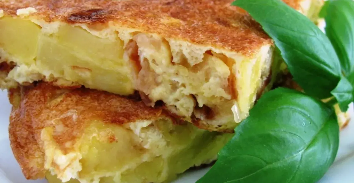 Pyszna tortilla de patatas, ze złotobrązową skórką i soczystym wnętrzem, ozdobiona świeżymi liśćmi bazylii.