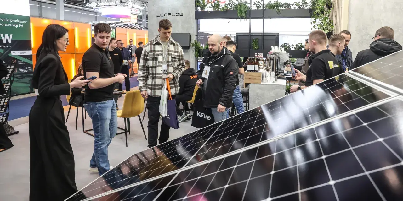 Ludzie zwiedzają targi energii odnawialnej, oglądając panele słoneczne i stoiska firm.