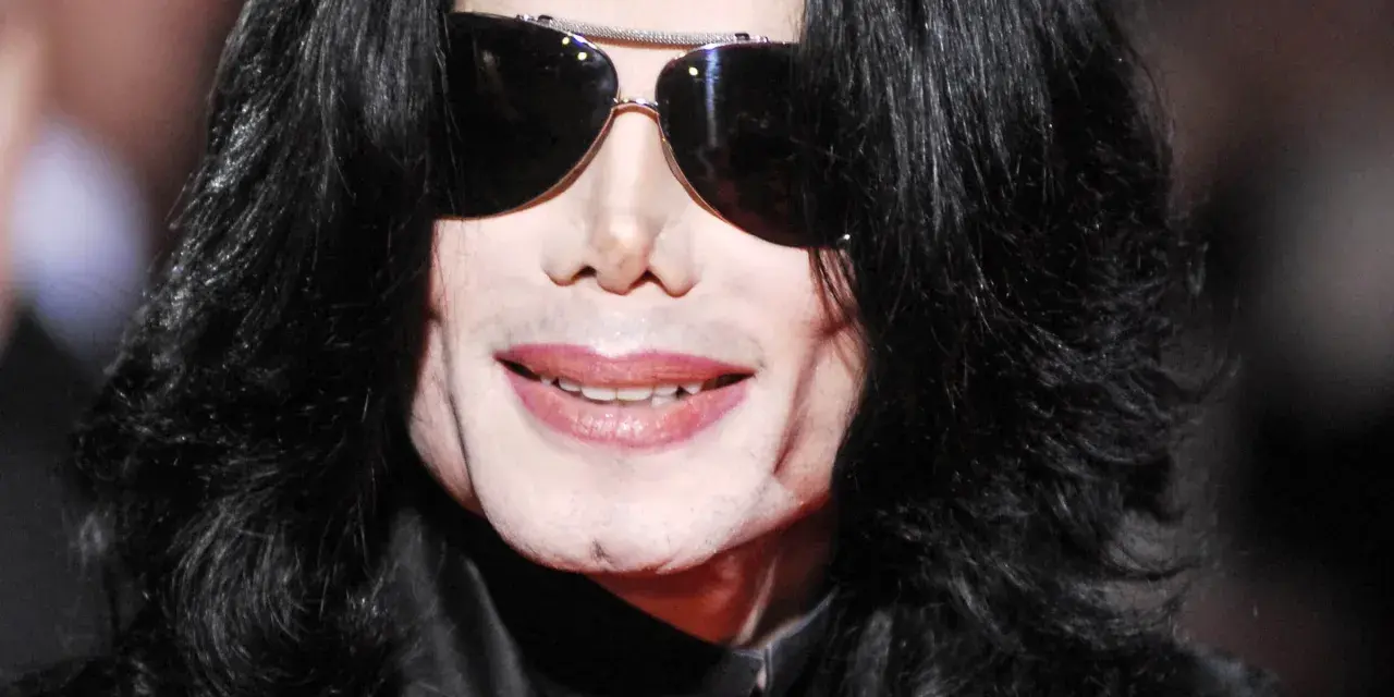 Michael Jackson w okularach przeciwsłonecznych i czarnych włosach. Jego uśmiech i twarz budzą pytania, jak zmarł Michael Jackson.