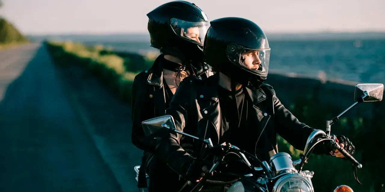 Coppia in moto romantica, con caschi neri, giacche di pelle, su una strada panoramica al tramonto.