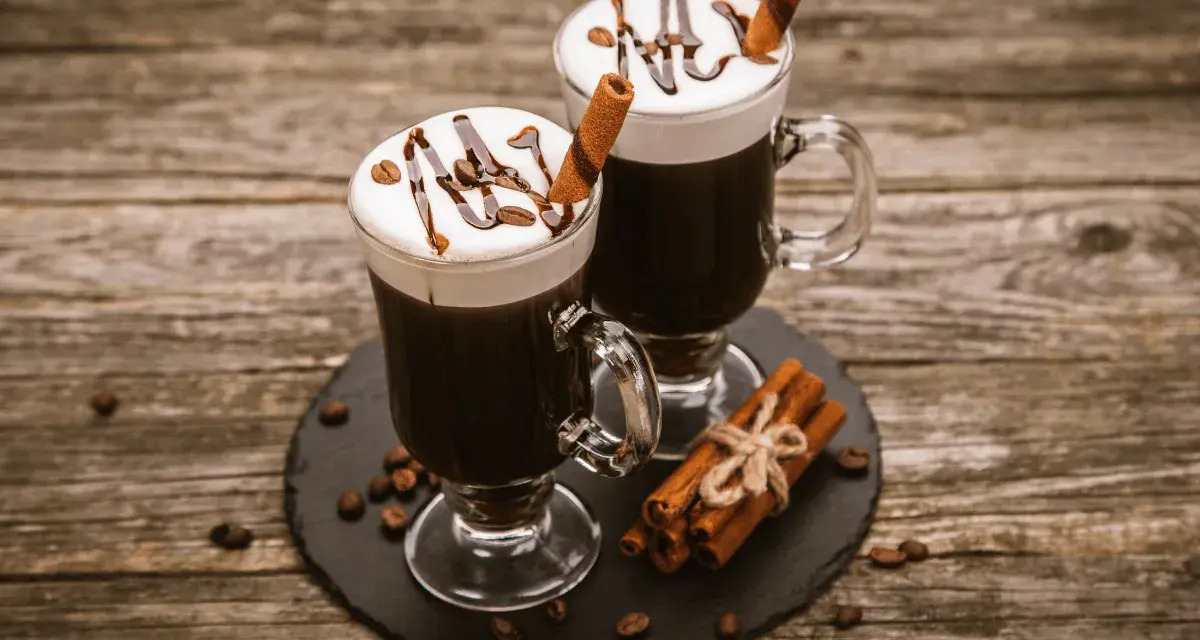 Dwa Irish coffee z bitą śmietaną, polewą czekoladową i laską cynamonu. Jaki to smak? Słodki, kawowy, z nutą alkoholu i przypraw.