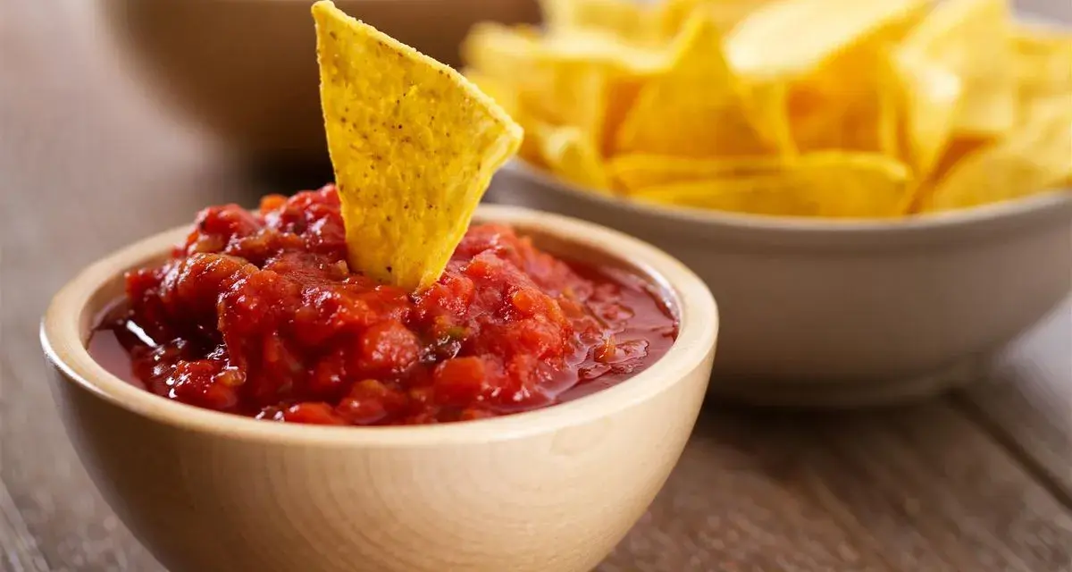Una tortilla croccante affonda in una ciotola di fresca salsa messicana per tortillas, con altre tortillas sullo sfondo.