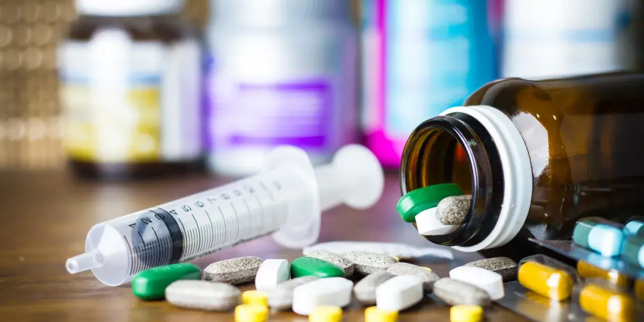 Leki, w tym zielone tabletki, rozsypane obok strzykawki i buteleczki. Może to być methocarbamol.