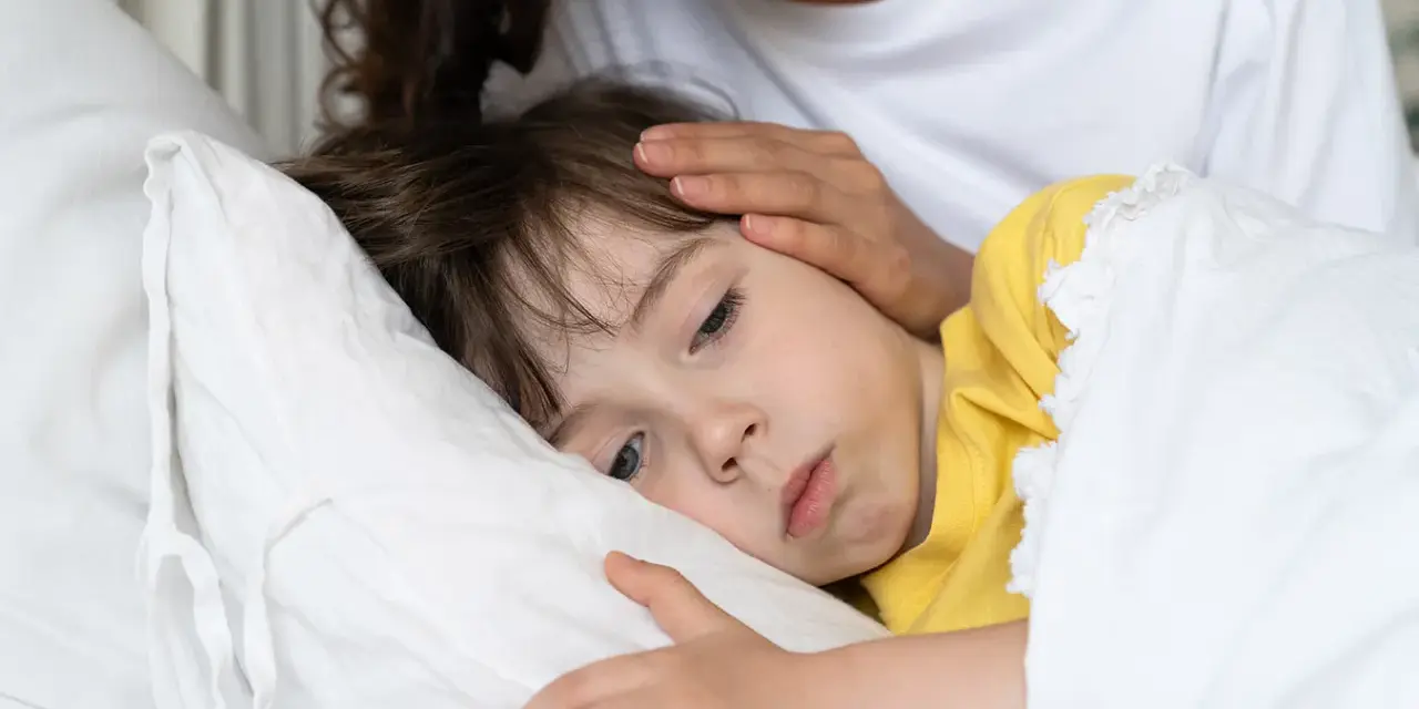Chore dziecko w łóżku, mama głaszcze je po czole. Warto pamiętać o odpowiednich paracetamol czopki dawki dla dzieci.