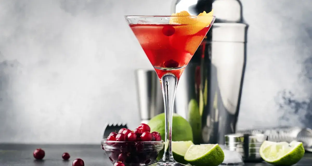 Elegancki cosmopolitan drink, gdzie zamiast żurawiny użyto świeżych owoców. Obok kieliszka stoją limonki i shaker.
