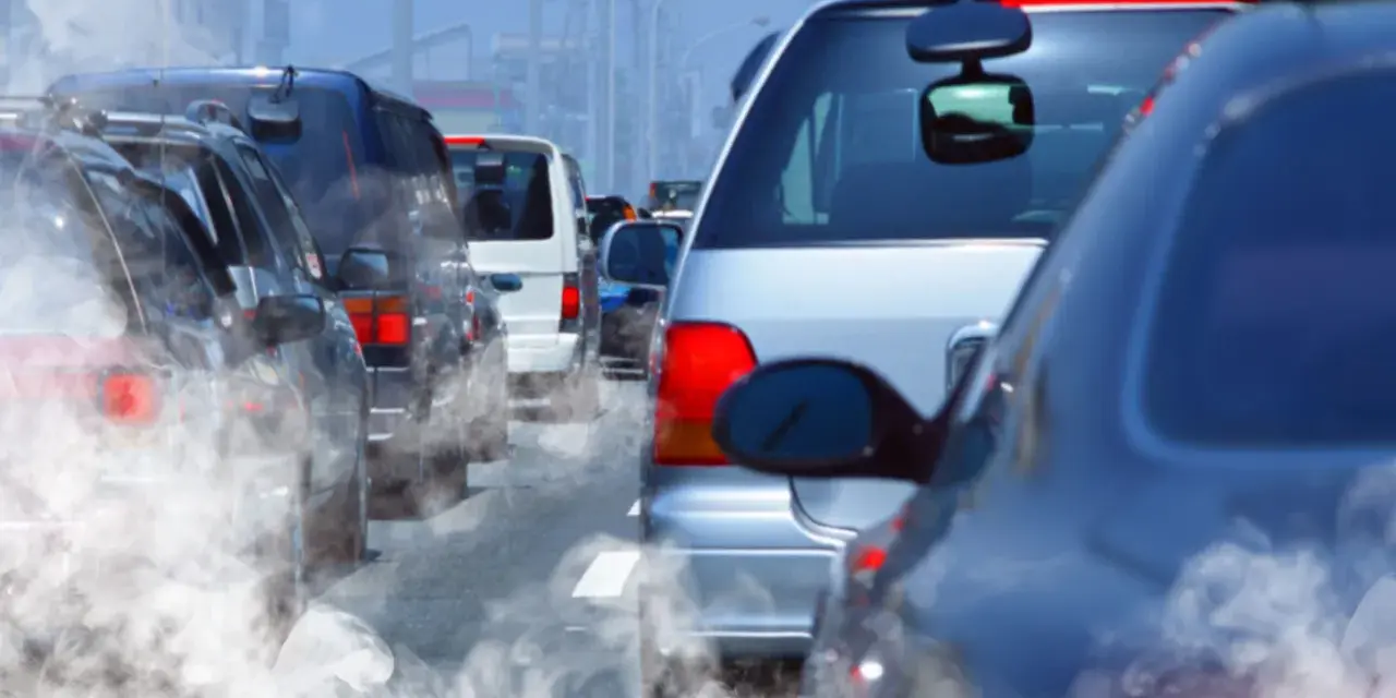 Tráfico denso con humo saliendo de los coches, reflejando la contaminación.