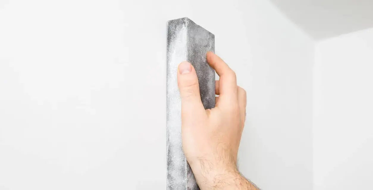 Mano lijando una pared blanca para reparar grietas en techo de yeso.