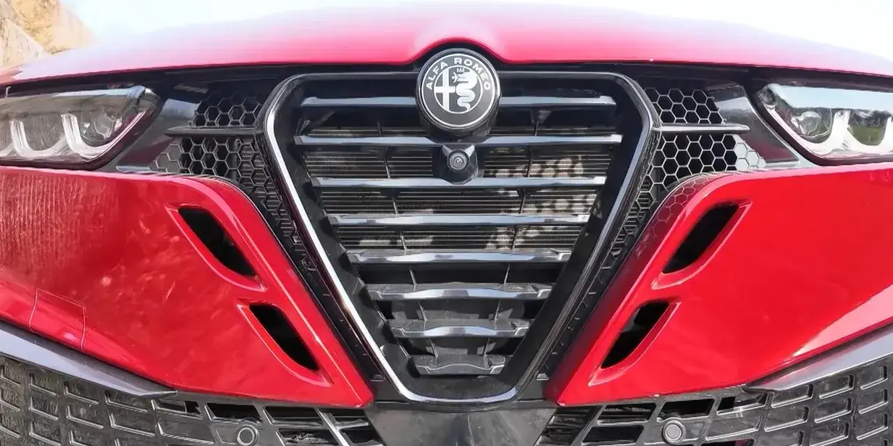 Czerwona Alfa Romeo z bliska. Widoczny grill w kształcie tarczy z logo, reflektory i detale karoserii w zbliżeniu. Alfa makro.