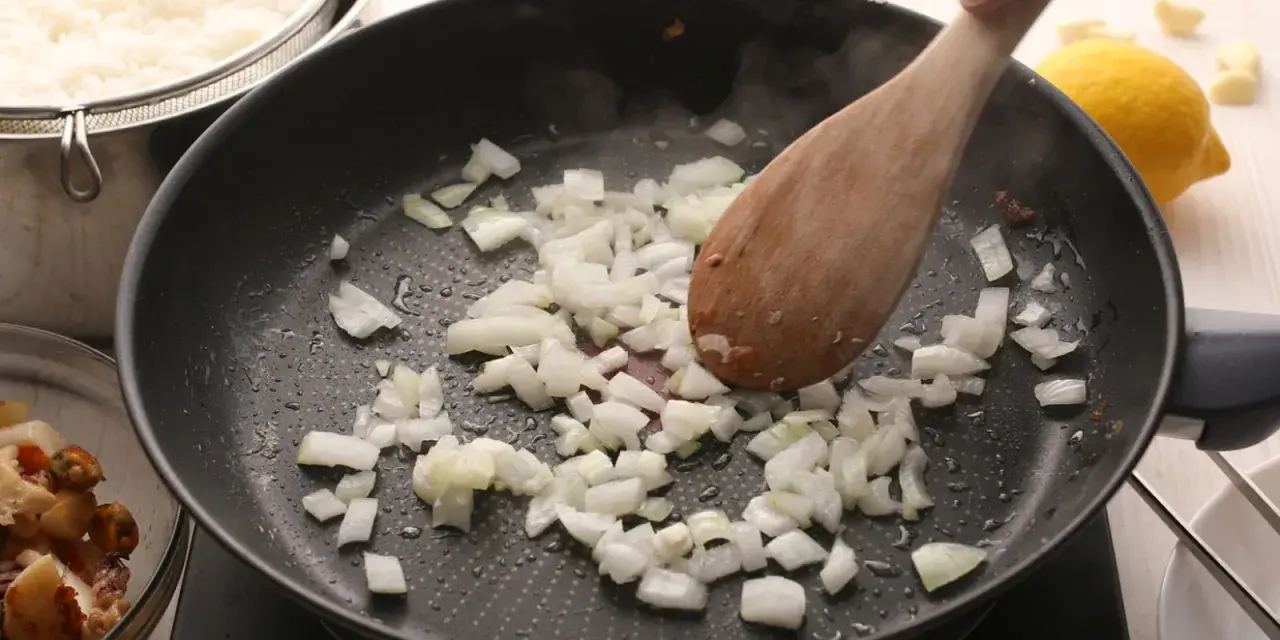 Cebolla picada se sofríe en una sartén, parte de unas deliciosas recetas con cebolla. Arroz blanco y mariscos esperan.