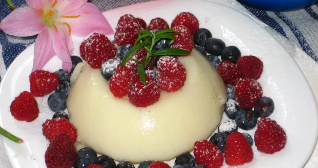 Panna cotta z malinami i borówkami, posypana cukrem pudrem. Idealny legumina przepis na deser.