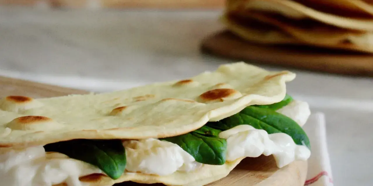 Piadina fatta in casa ripiena di mozzarella filante e spinacini freschi, pronta per essere gustata.