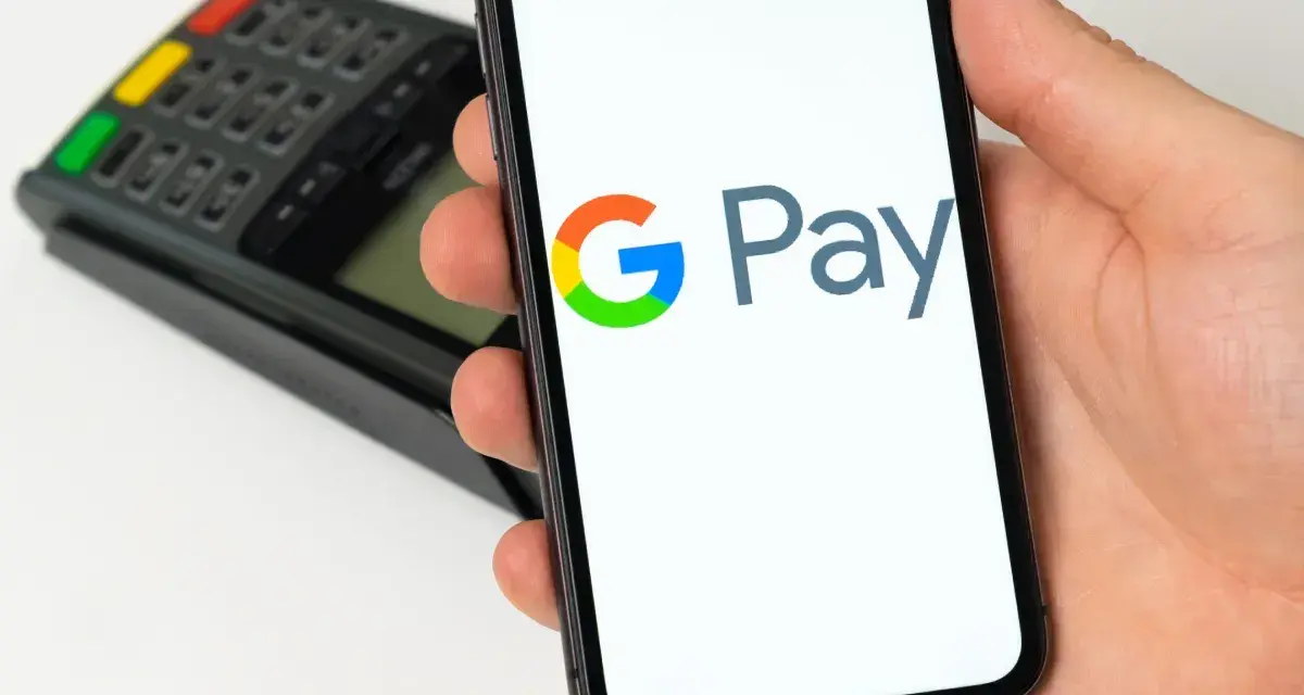 Dłoń trzyma smartfon z widocznym logo Google Pay. W tle terminal płatniczy. Szybkie i wygodne płatności.