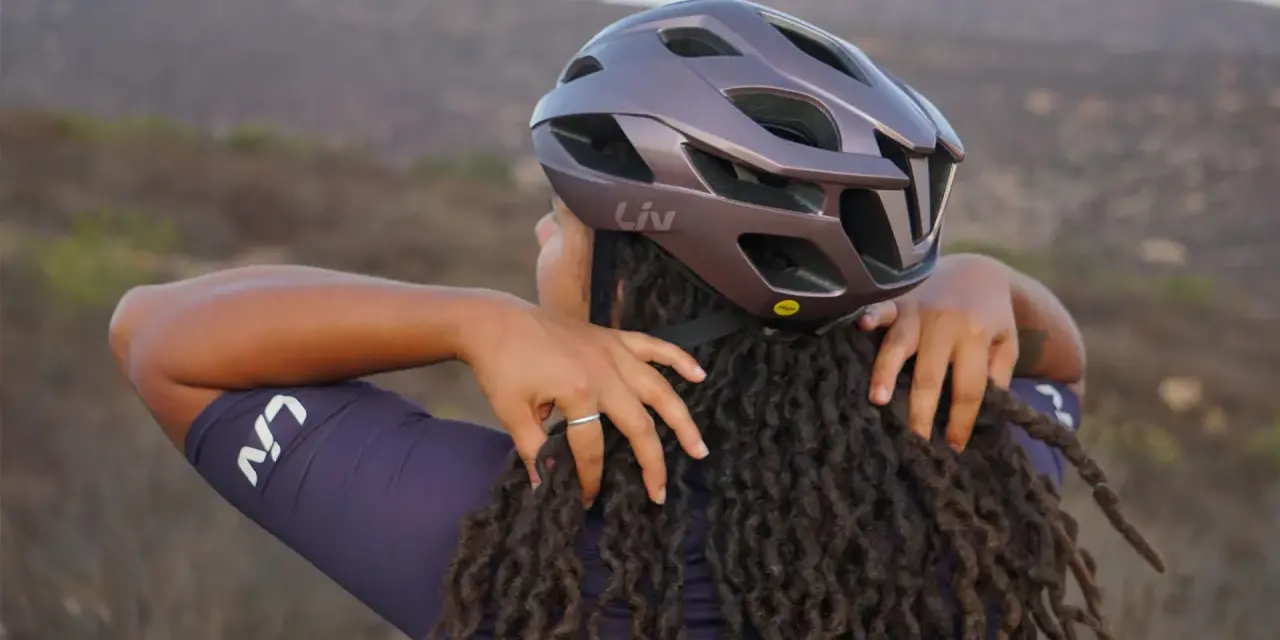 Donna con dreadlocks che regola un casco da bici Liv. Non preoccuparti se il tuo casco è stretto, ci sono modi per allargare il casco stretto.