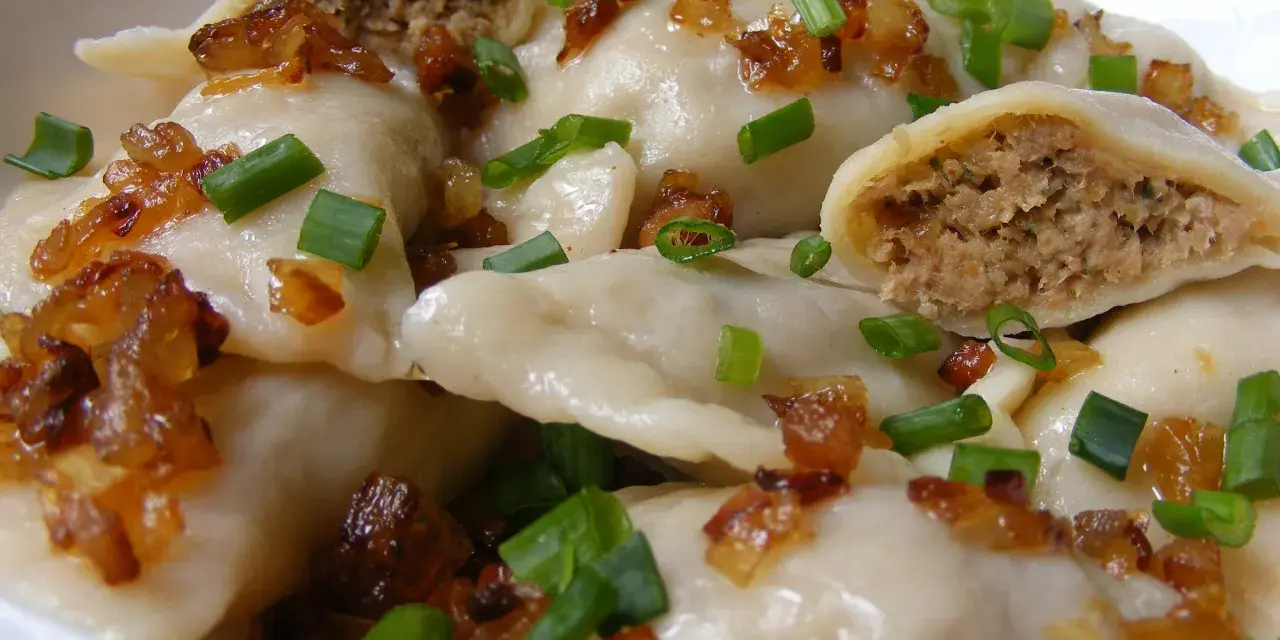 Domowe pierogi z mięsem, posypane smażoną cebulką i szczypiorkiem.