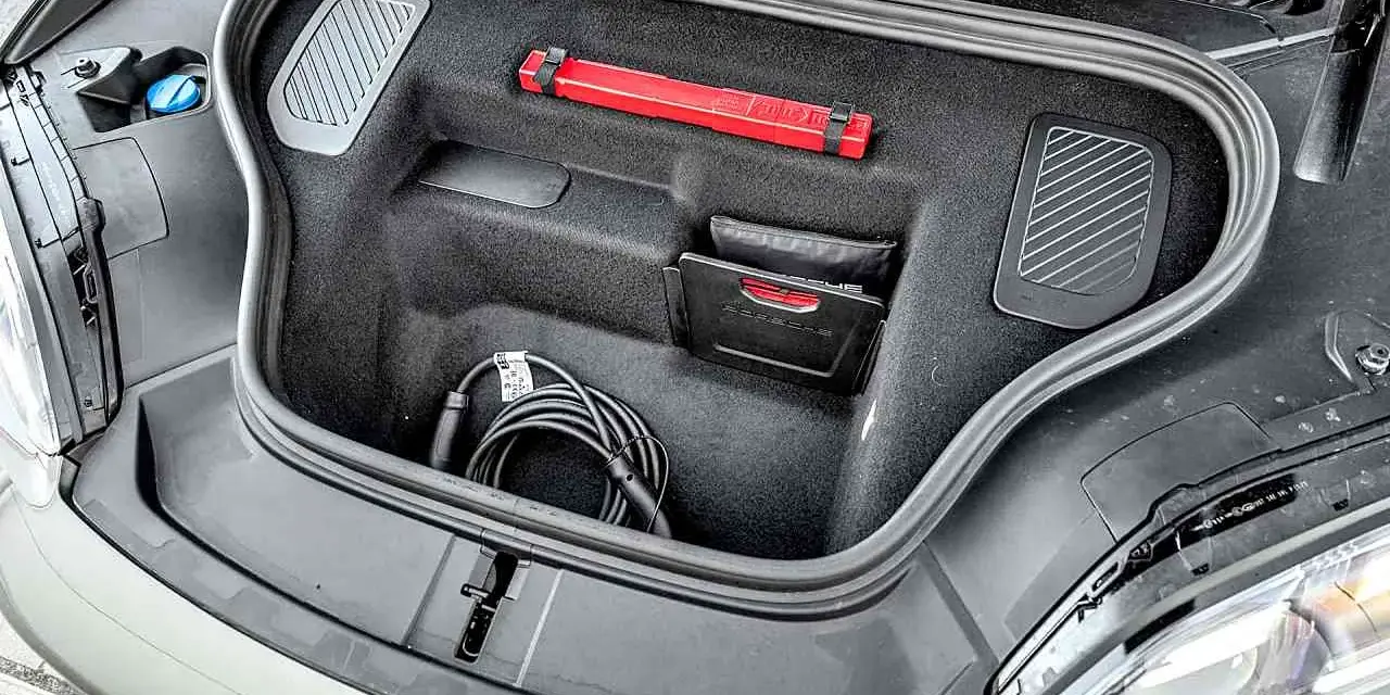 Otwarty bagażnik Porsche Macan z kablem do ładowania, apteczką i instrukcją.