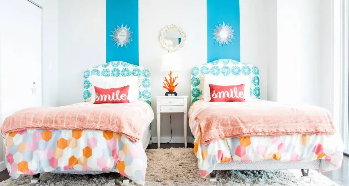 Dos camas gemelas en habitación pequeña, con cabeceros estampados y colchas naranjas. ¡Una solución genial para como poner dos camas en una habitacion pequeña!