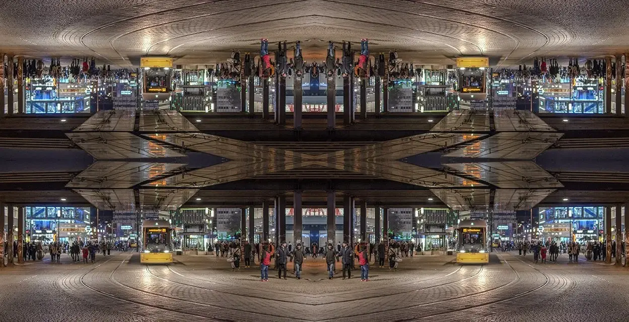 Nocne miasto z żółtym tramwajem i ludźmi. Kompozycja symetryczna tworzy surrealistyczny, odbity świat.