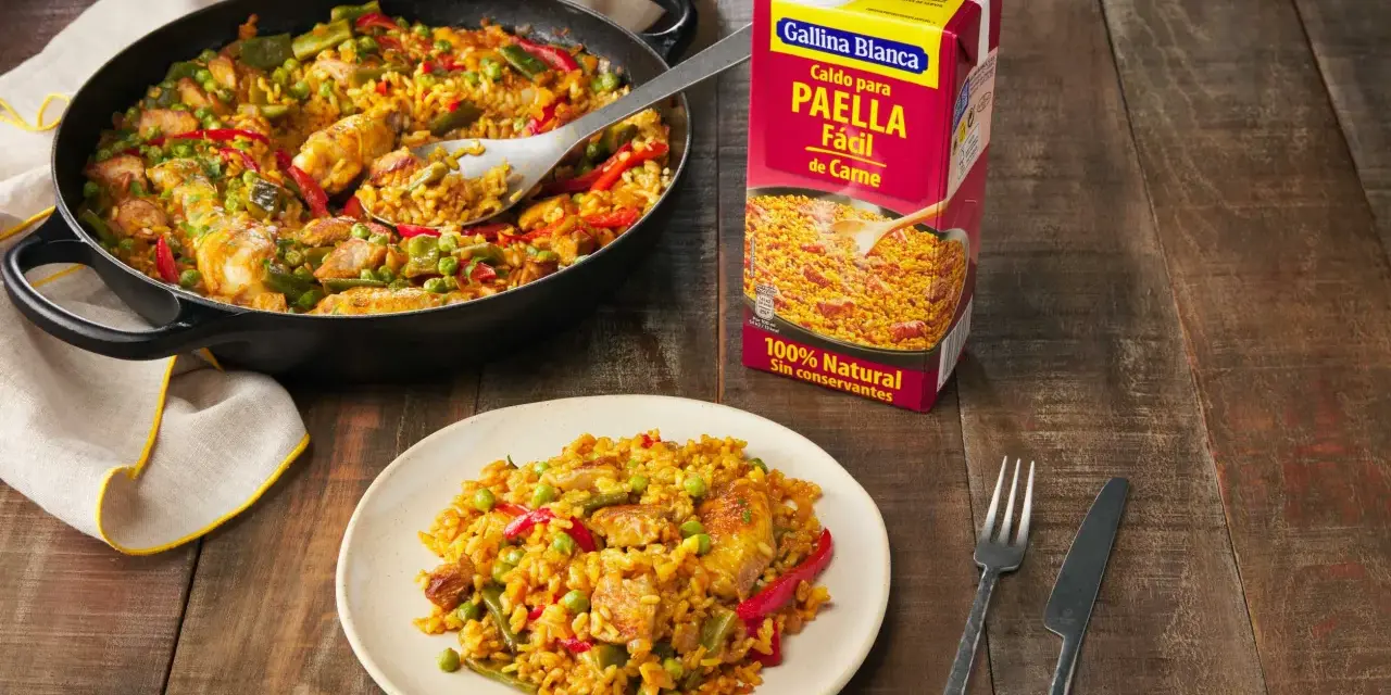 Paella de carne recién hecha en sartén y plato, lista para disfrutar. Un caldo Gallina Blanca para paella fácil de carne a su lado.