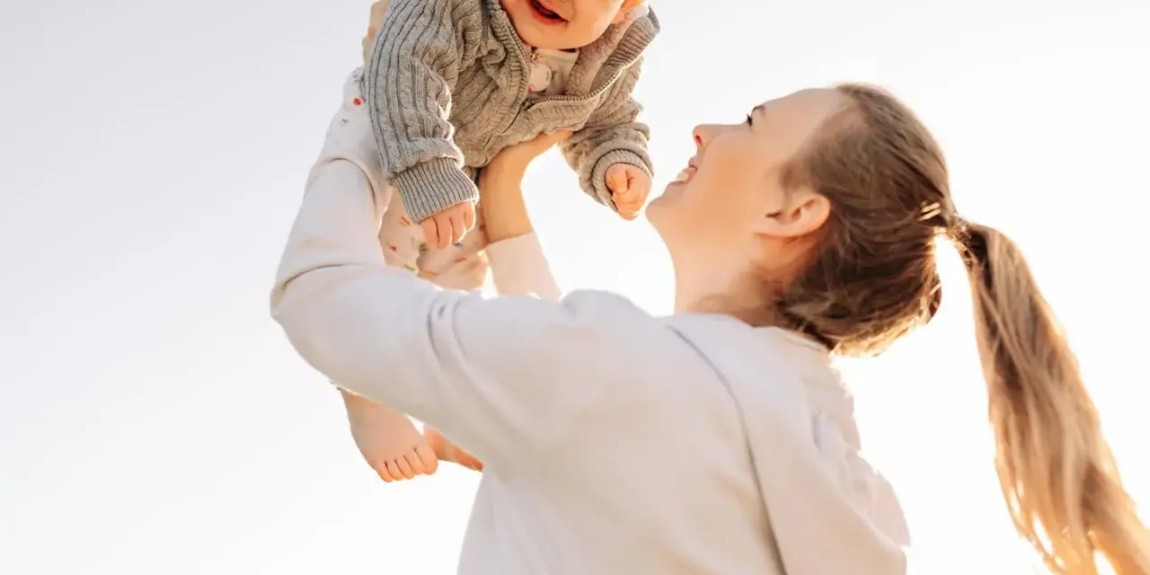 Mutter wirft ihr lachendes Baby in die Luft. Ein fröhlicher helikopter-mutter test im Freien.