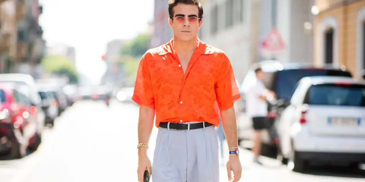 Hombre con camisa naranja estampada y pantalones grises, luciendo un elegante french tuck.