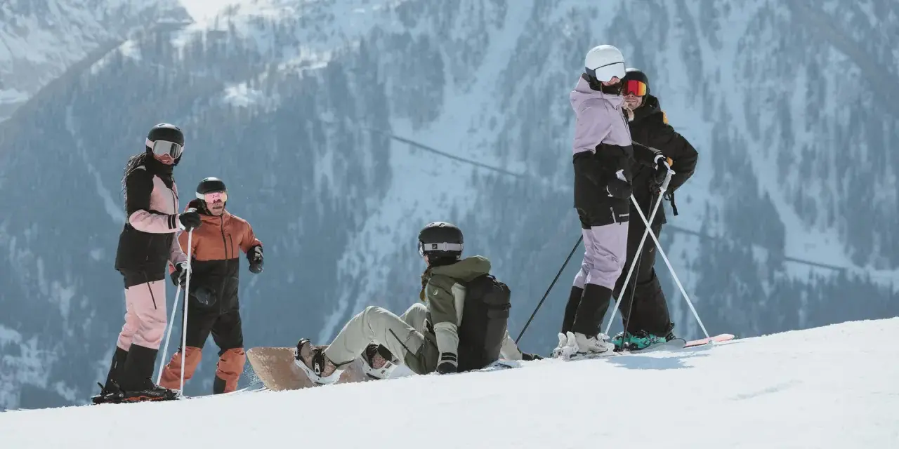 Grupa narciarzy i snowboardzistów odpoczywa na stoku, podziwiając majestatyczne góry Sierra Nevada.