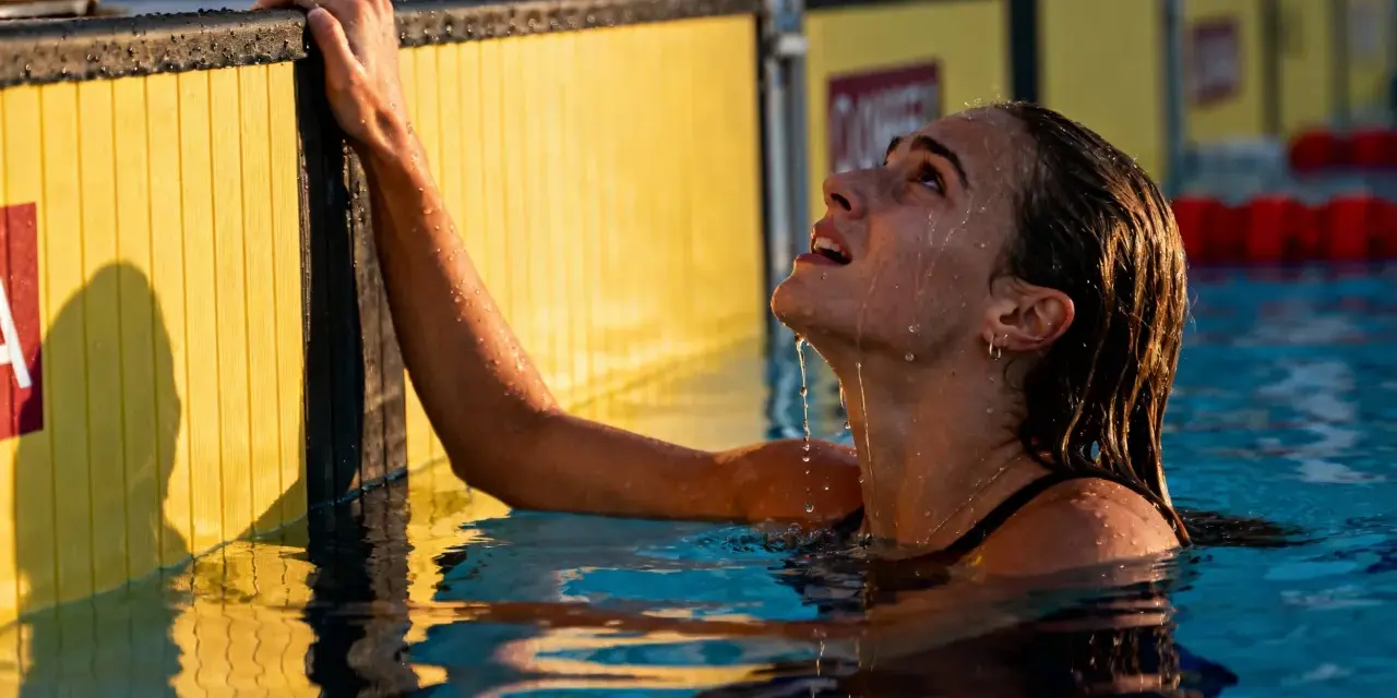 Nuotatrice con gocce d'acqua sul viso, aggrappata al bordo giallo della piscina. Si può fare il bagno in piscina con il ciclo, senza problemi.