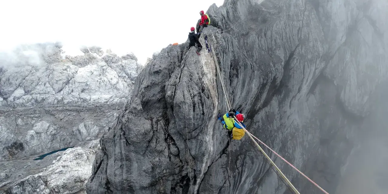 Wspinaczka na Piramidę Carstensza. Alpinista z plecakiem zjeżdża po linie, podczas gdy inni czekają na szczycie.