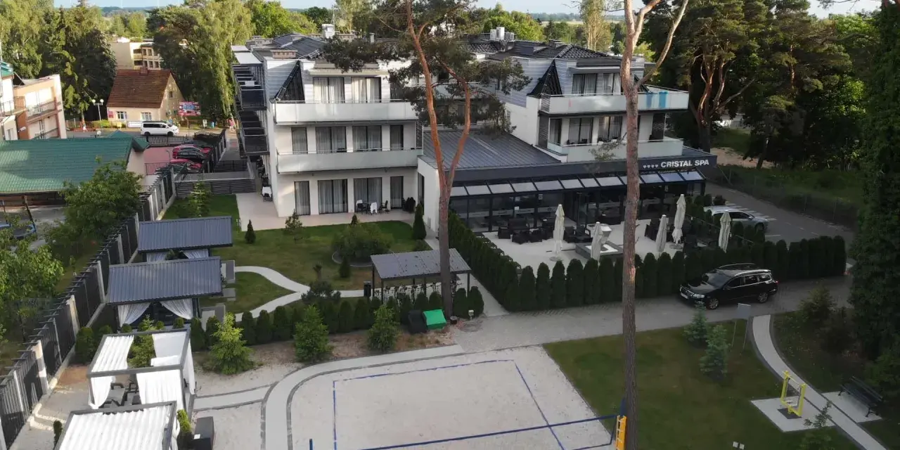 Nowoczesny hotel Cristal Spa z basenem i kortem do siatkówki plażowej, otoczony zielenią.