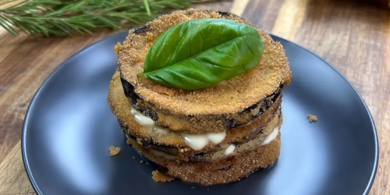 Deliziose cotolette di melanzane impilate, farcite con formaggio cremoso e guarnite con una foglia di basilico fresco.